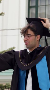 Şapkalı ve cüppeli modern mezun çocuk. Genç adam, üniversiteden başarılı bir şekilde mezun olan öğrencilerin mezuniyet töreninden birkaç dakika sonra aileleri ve arkadaşlarıyla konuşuyor.