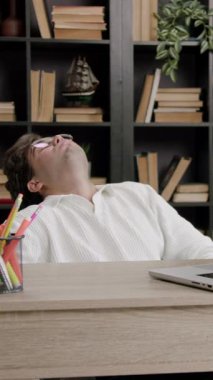 Disappointed boy leans back on chair at office table. Young man disappointed and angry because he fails a project for college. Student preparing for university on computer