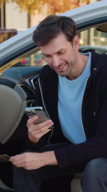Genç adam akıllı telefonunu online ödemeler için kullanıyor. Bir kredi kartı tutuyor ve kiralık arabanın parasını ödemek için telefonda ayrıntıları giriyor. Adam internetten banka kartı ve satın alınan arabanın telefonu ile ödeme yapıyor.