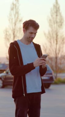 Şahıs, araçlarla çevrili bir otoparktaki araba paylaşım servisine ulaşmak için akıllı telefonuyla etkileşime girer ve gün batımının ılık ışığıyla aydınlatılır.