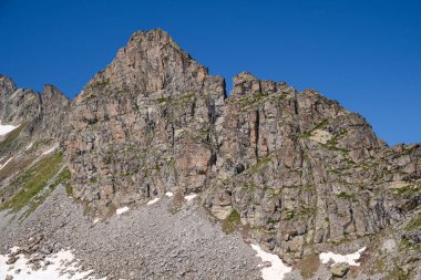 İtalyan Alpleri 'nde dik, kayalık uçurumlar ve karla kaplı engebeli dağ zirveleri. Açık mavi gökyüzü araziyle çelişiyor..