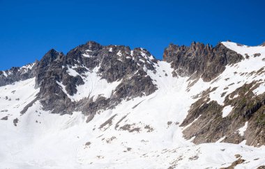 Rocky tepeleri parlak mavi gökyüzüne karşı keskin bir şekilde yükselir, yamaçları taze karla kaplanır, Vermiglio 'nun kış manzarasının güzelliğini gözler önüne serer..