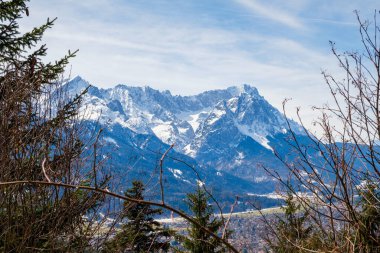 Kış boyunca Garmisch-Partenkirchen, Bavyera 'da karla kaplı görkemli dağ zirveleri doğanın güzelliğini gözler önüne seriyor. Ağaçların çevresini çevreleyen bu nefes kesici dağ manzarası berrak bir gökyüzünün altında.