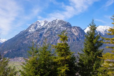 Kış boyunca Garmisch-Partenkirchen 'de görkemli karla kaplı tepeler ufuk çizgisine hakim. Yeşiller yemyeşil ağaçlar ön planda, mavi gökyüzüne karşı çarpıcı bir kontrastlık oluşturuyor..