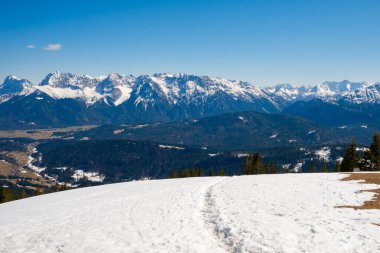 Garmisch-Partenkirchen 'in zeminini kaplayan karlar, berrak mavi gökyüzünün altından yükselen görkemli dağlar gibidir. Kış manzarası doğanın güzelliğini keşfetmeye ve takdir etmeye davet eder..