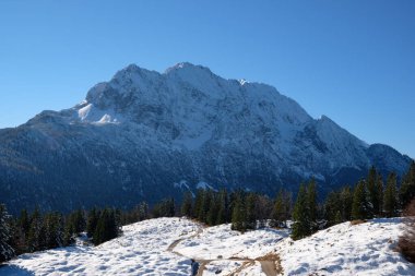 Mittenwald, Bavyera yakınlarındaki görkemli dağları kar örtüyor ve çarpıcı bir kış manzarası yaratıyor. Açık mavi gökyüzü yükselen tepelerin ve etrafındaki çam ağaçlarının güzelliğini arttırır..