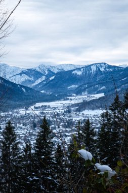 Bavyera 'nın Tagernsee kentindeki görkemli dağlarla çevrili köyü kar örtüyor. Çam ağaçları dimdik durur, gökyüzünün yumuşak bir buluta işaret ettiği gibi güzel bir kış sahnesi yaratır..