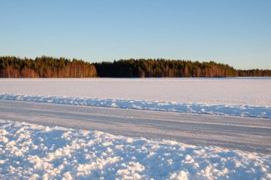 Mora 'da huzurlu bir kış günü, Dalarna donmuş bir gölle birlikte engin bir kar bulutunu gözler önüne seriyor. Uzun ağaçlar, berrak mavi gökyüzünün altındaki ufuk çizgisinde sakin bir atmosfer yaratıyor..