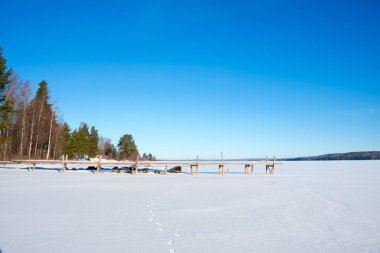 A serene winter landscape in Vastanvik, Dalarna reveals a frozen lake under clear blue skies. clipart