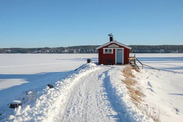 Dalarna 'nın Vastanvik kentindeki dingin donmuş göl ve kış manzarasıyla çevrili, kapısına kadar uzanan karlı bir yolda huzur içinde duran küçük bir kırmızı kulübe, sakin atmosferi yükseltiyor..