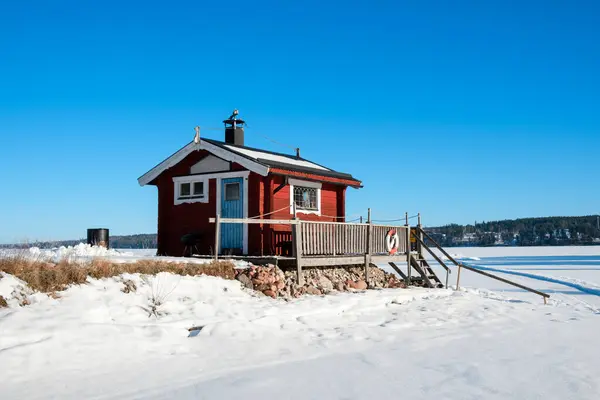 Vastanvik, Dalarna 'da donmuş bir gölün yanında büyüleyici kırmızı bir kulübe duruyor. Kar toprağı kaplıyor ve berrak mavi gökyüzü sakin kış manzarasını tamamlıyor..