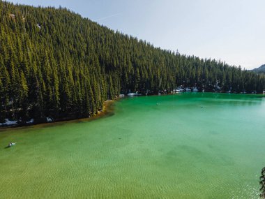 Oregon, Devils Gölü 'ndeki kanocu. Kıyılarda kar var. Algae 'den Yeşil Göl. Drone fotoğrafı.