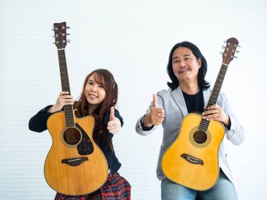 Beyaz arka planda oturan Asyalı ikili gitaristlerin portresi müzik, sanatçı ve müzisyen konsepti için alkış işaretlerini gösteriyor.