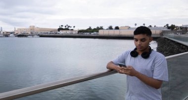 Genç çocuk deniz kenarındaki cep telefonuna bakıyor.