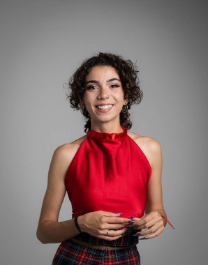 Kıvırcık saçlı kız gülümser ve kameraya bakar. Renkli kırmızı elbiseler giyiyor. Boşluğu kopyala