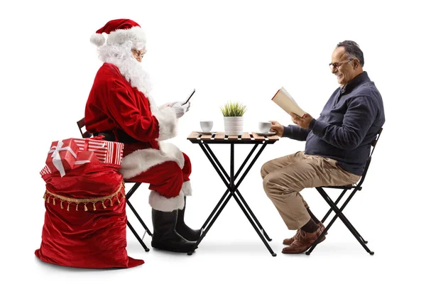 Święty Mikołaj Przy Użyciu Smartfona Dojrzałego Mężczyzny Siedzącego Przy Stole — Zdjęcie stockowe