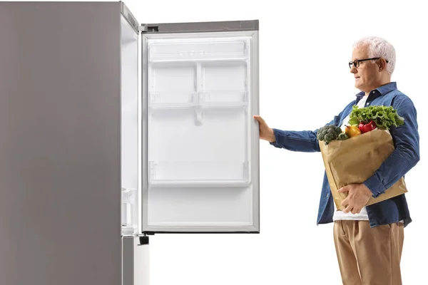 白地に隔離された冷蔵庫を開ける食料品袋を持つ成熟した男のプロフィール — ストック写真