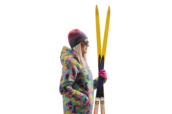 一个穿着滑雪裤和夹克的女人拿着一双白色背景的滑雪板的侧面照 — 图库照片
