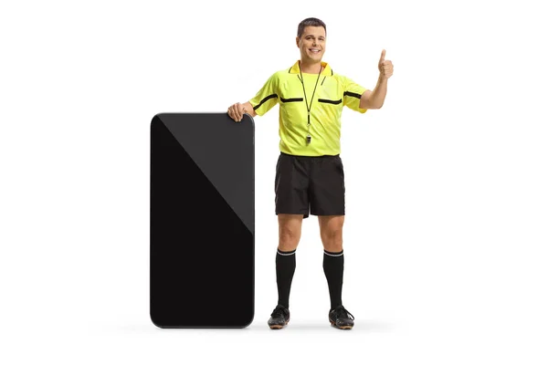一个足球裁判员站在一个大智能手机旁边的全长肖像 用白色背景把他的大拇指伸出来做手势 — 图库照片