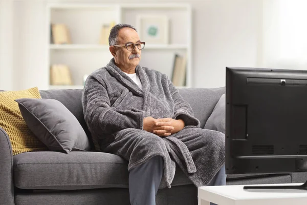 Зрелый Мужчина Халате Сидит Сером Диване Смотрит Телевизор Дома — стоковое фото