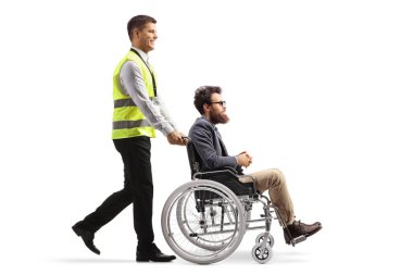 Bir havaalanı çalışanının beyaz arka planda izole edilmiş tekerlekli sandalyeli bir adamı yürürken ve iterken tam boy profil çekimi.