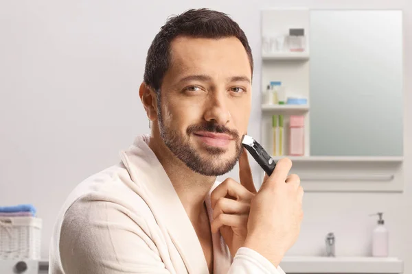 Joven Sonriente Con Albornoz Recortando Barba Dentro Baño —  Fotos de Stock