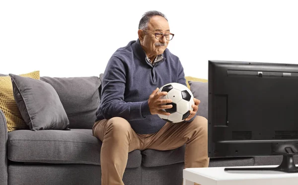 Dojrzały Mężczyzna Siedzi Kanapie Trzymając Piłkę Nożną Oglądając Jego Zespół — Zdjęcie stockowe