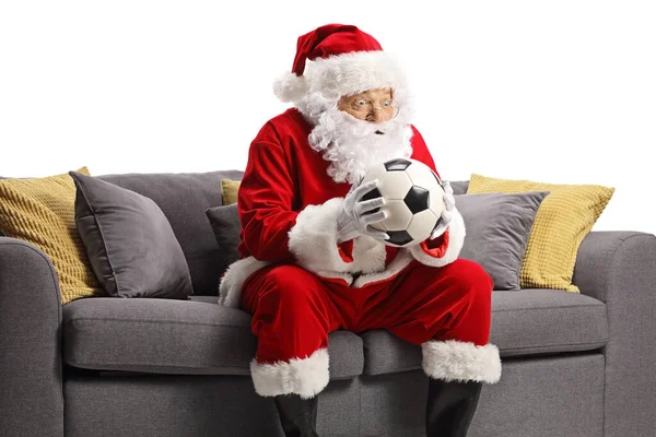 Surpreendido Papai Noel Segurando Uma Bola Futebol Sentado Sofá Isolado — Fotografia de Stock
