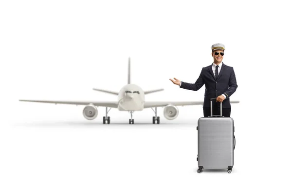 飛行機の前にスーツケースが立っていて 白い背景に手で指差すパイロット — ストック写真
