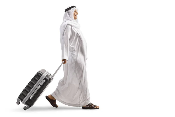 フル長さプロファイルショットのアラブ人の男で民族服を歩くと白い背景に隔離されたスーツケースを引っ張る — ストック写真