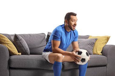 Spor formalı genç adam bir top tutuyor ve televizyonda beyaz arka planda izole edilmiş futbol seyrediyor.