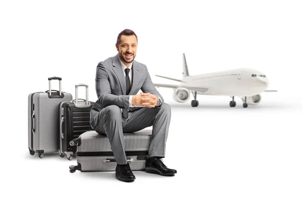 白い背景に隔離された航空機の前のスーツケースに座っているビジネスマン — ストック写真
