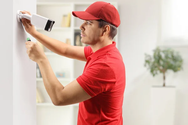 Profile shot of a young man installing a security camera on a wall in a room