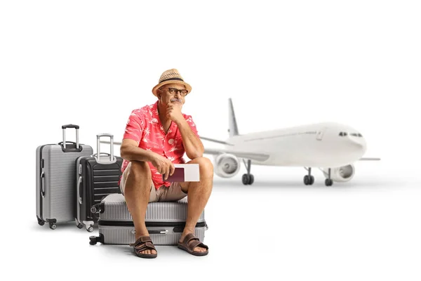 スーツケースに座って白い背景に隔離された飛行機の前で待っている熟女観光客 — ストック写真