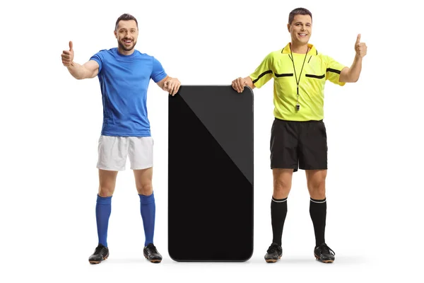 一个裁判和一个足球运动员站在一个大手机旁边 用一个白色背景的大拇指做手势的全长肖像 — 图库照片