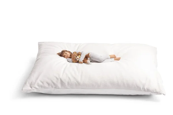 穿着睡衣的小女孩抱着泰迪熊睡在白色背景的柔软的大枕头上 — 图库照片