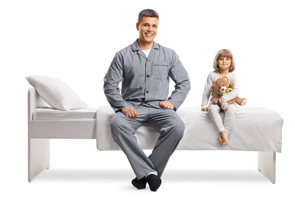 若いです男と小さな女の子でパジャマで座っていますベッドの上に隔離された白い背景 — ストック写真