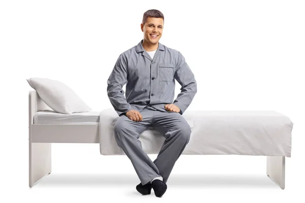 Glimlachende Jongeman Pyjama Zittend Een Bed Geïsoleerd Witte Achtergrond — Stockfoto