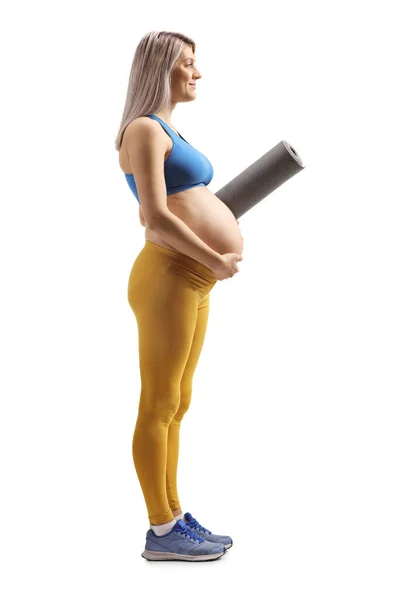 白い背景に隔離された運動マットを保持しているスポーツウェアの妊婦のフル長プロファイルショット — ストック写真