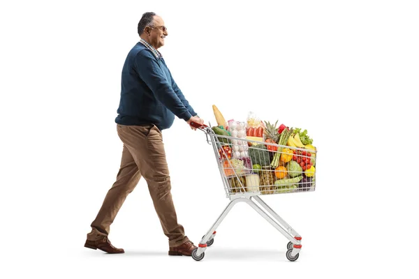 白い背景に隔離されたショッピングカートで食べ物と一緒に歩く成熟した男の完全な長さのプロフィールショット — ストック写真