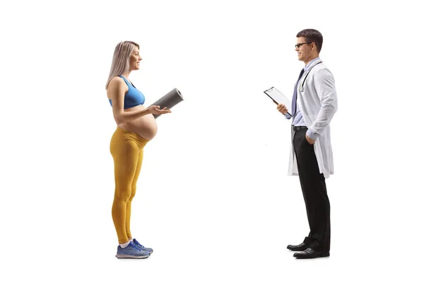 一名穿着运动服 拿着运动垫 与一位白种人隔离的医生交谈的孕妇的全景照片 — 图库照片