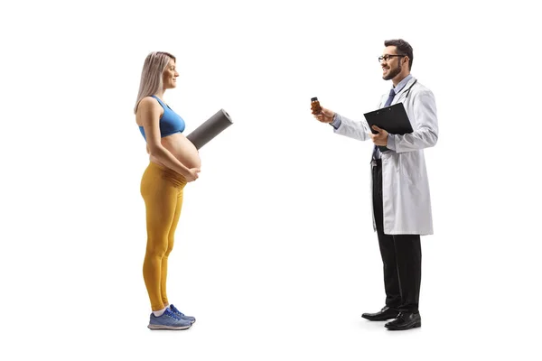 白い背景に隔離されたスポーツウェアの妊婦にビタミンのボトルを与える医師の完全な長さのプロフィールのショット — ストック写真