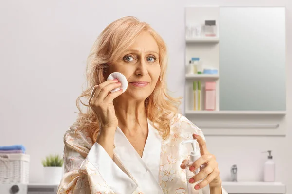 一个成熟的女人在浴室里用棉垫和润肤面来清洁她的脸 — 图库照片