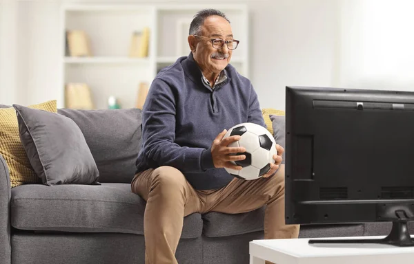 Dojrzały Mężczyzna Trzyma Piłkę Nożną Siedzi Kanapie Oglądając Mecz Telewizji — Zdjęcie stockowe