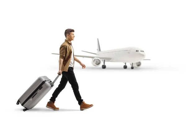 白い背景に隔離された飛行機の前で若い男性の乗客の歩行とスーツケースを引くの完全な長さのプロフィールショット — ストック写真
