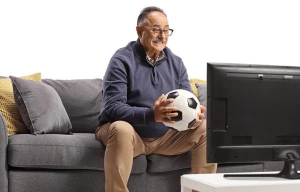 サッカーボールを持っている成熟した男を混乱させ 白い背景に隔離されたテレビで試合を見てソファに座って — ストック写真