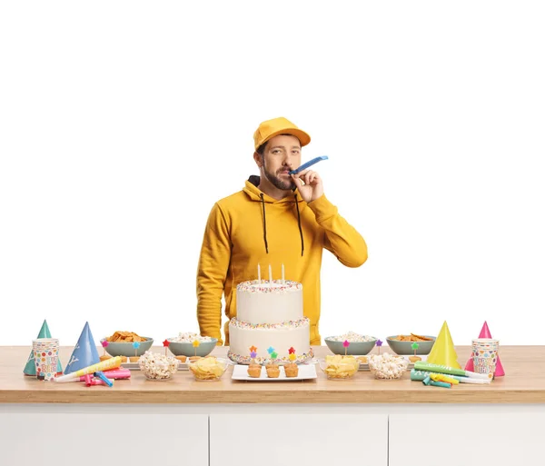 男吹いているパーティーホーン後ろにカウンターとともにケーキ隔離された白い背景 — ストック写真