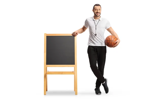 体育教師はバスケットボールを持ち 白地に隔離された黒板にもたれている — ストック写真
