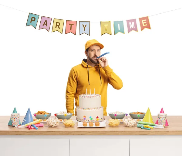 Casual Young Man Blowing Horn Counter Cake Favors Flags Text — Stock Photo, Image