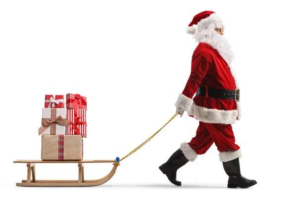Santa Claus拖着一个木制雪橇拉着白色背景的礼物拍摄的全长侧面照片 — 图库照片